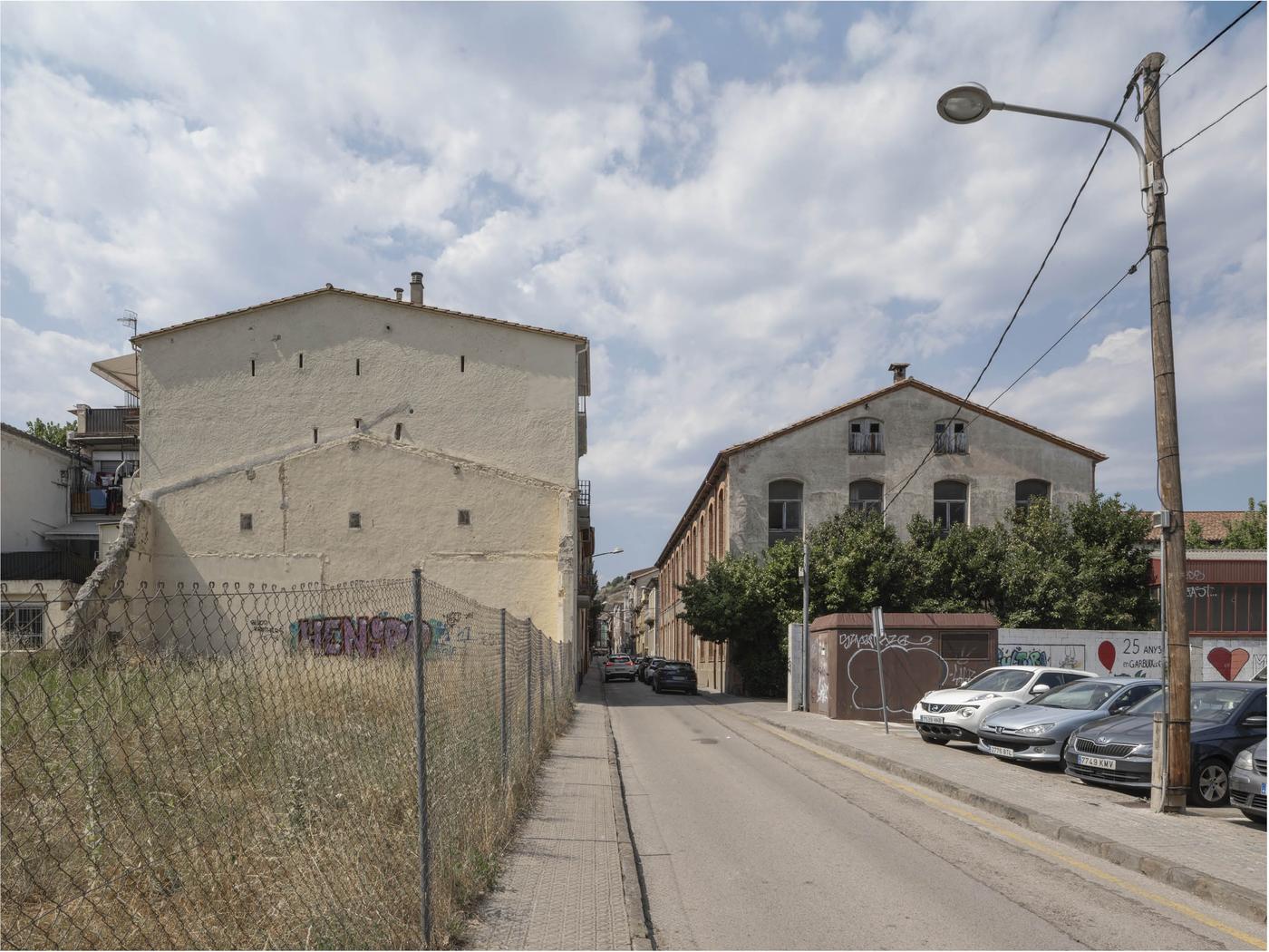 Calle de Olot con medianera ciega y fábrica al fondo